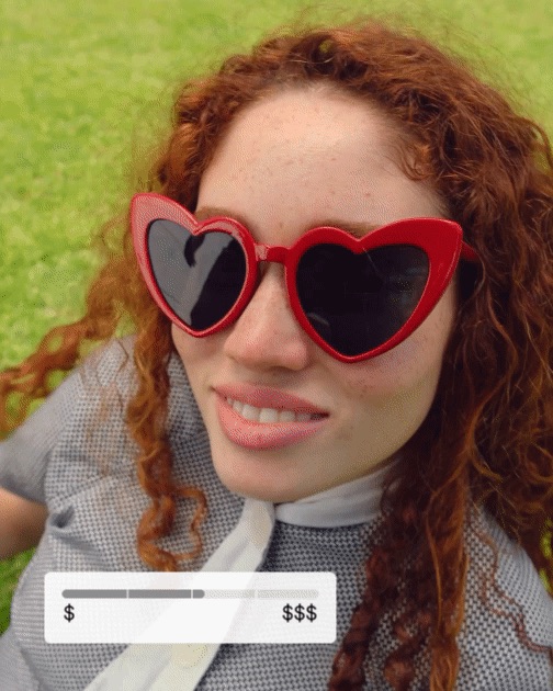 Image of a red headed woman smiling with heart shaped sunglasses that are red